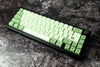 Mechanisch toetsenbord met pastelgroene matcha keycaps en subtiele donkere accenten, inclusief een unieke toets met matcha-symbool, op een zwart-wit gemarmerd bureaublad.
