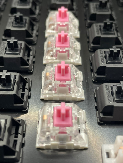 Close-up row of Kailh Speed Pink switches mounted in a switch tester with black Gateron housings in the background.