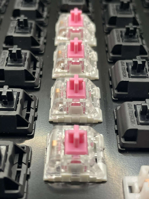 Close-up row of Kailh Speed Pink switches mounted in a switch tester with black Gateron housings in the background.