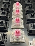 Close-up row of Kailh Speed Pink switches mounted in a switch tester with black Gateron housings in the background.