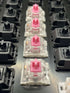 Close-up row of Kailh Speed Pink switches mounted in a switch tester with black Gateron housings in the background.