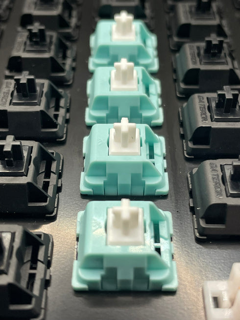 Vijf KTT Mint switches gemonteerd op een toetsenbord tussen zwarte switches – bovenaanzicht